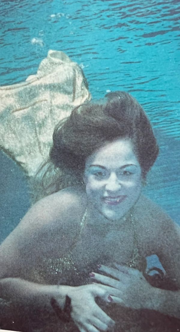 Smiling mermaid swimming underwater in costume.