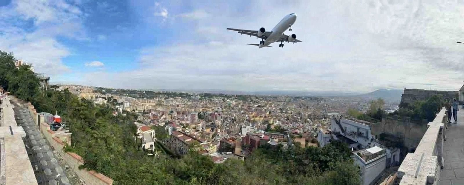 Airplane flying over a sprawling city with greenery and clear skies.