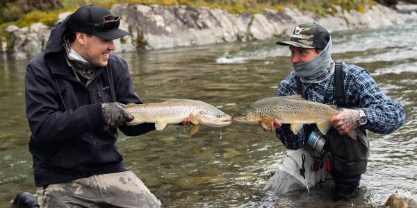 Two men holding large fish in a river.