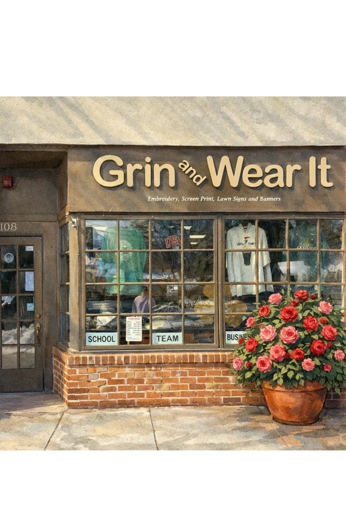 Exterior of 'Grin and Wear It' clothing and embroidery shop with a flower pot outside.