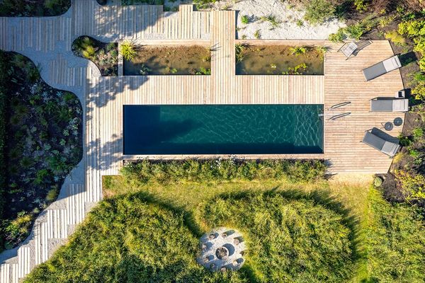 Aerial view of a rectangular pool with wooden deck and surrounding greenery.