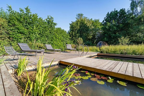 Outdoor wooden deck with lounge chairs by a pond and greenery.