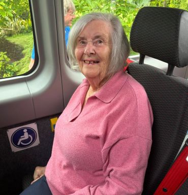 Elderly woman in pink sweater smiles while sitting in a vehicle with a wheelchair sign.