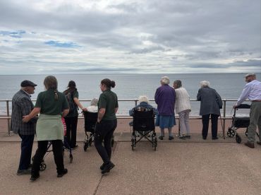 Group of elderly people and caregivers by the seaside on a cloudy day.