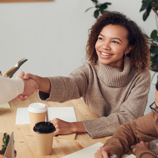 A woman smiling and shaking hands across a table in a casual meeting.