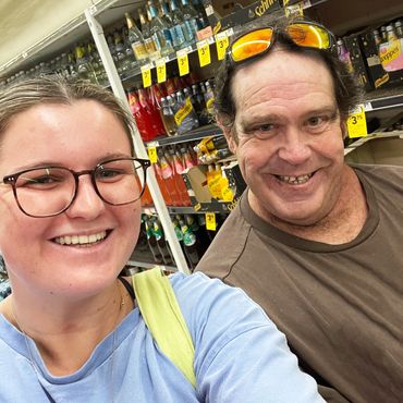 Two people smiling for a selfie in a store aisle with beverages.