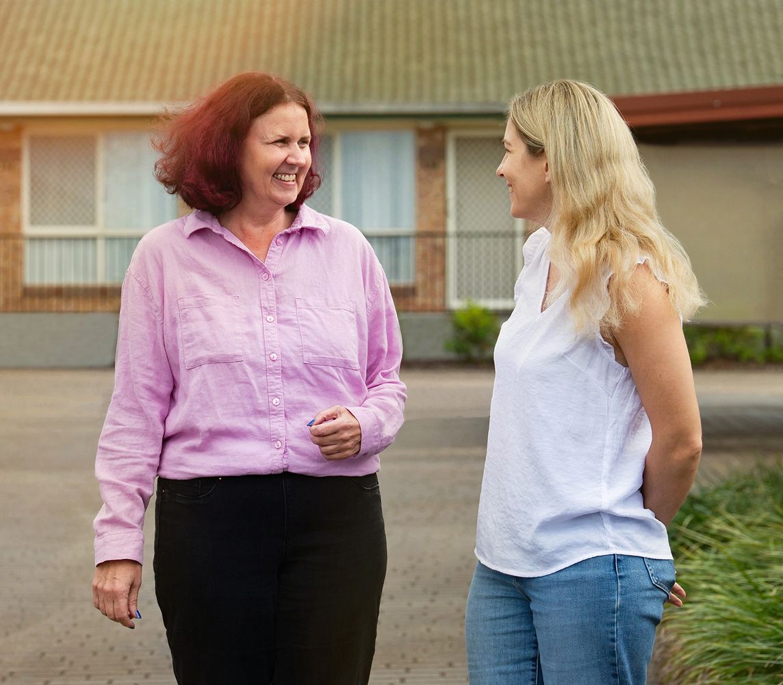 Two women smiling and chatting outside a residential building.