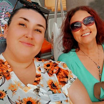 Two smiling women taking a cheerful selfie, one wearing sunflower print and the other with sunglasses.