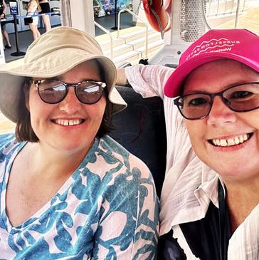 Two smiling women wearing hats and glasses, enjoying a sunny day outdoors.