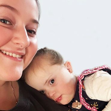 A smiling woman lovingly holds a resting baby with Down syndrome.