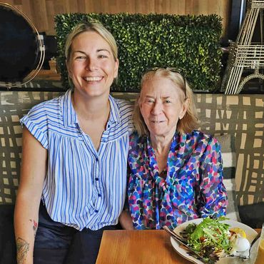 Two women smiling together at a dining table with a salad.