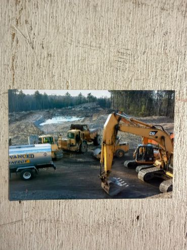 Construction vehicles at a muddy site with a small pond and trees in the background.