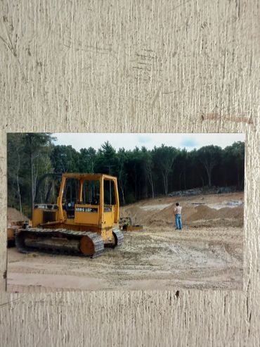 Yellow bulldozer and a man on a dirt construction site near trees.