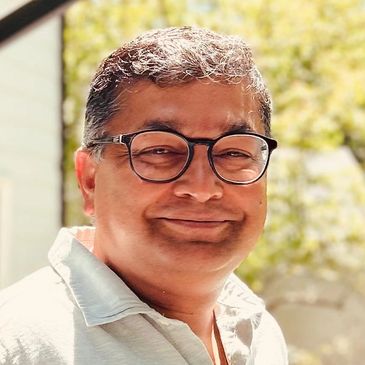 Smiling man with glasses in bright outdoor light.