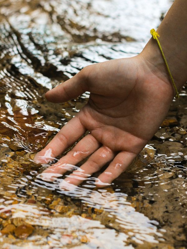 Hand gently touching flowing water, symbolising calm, connection, and emotional healing