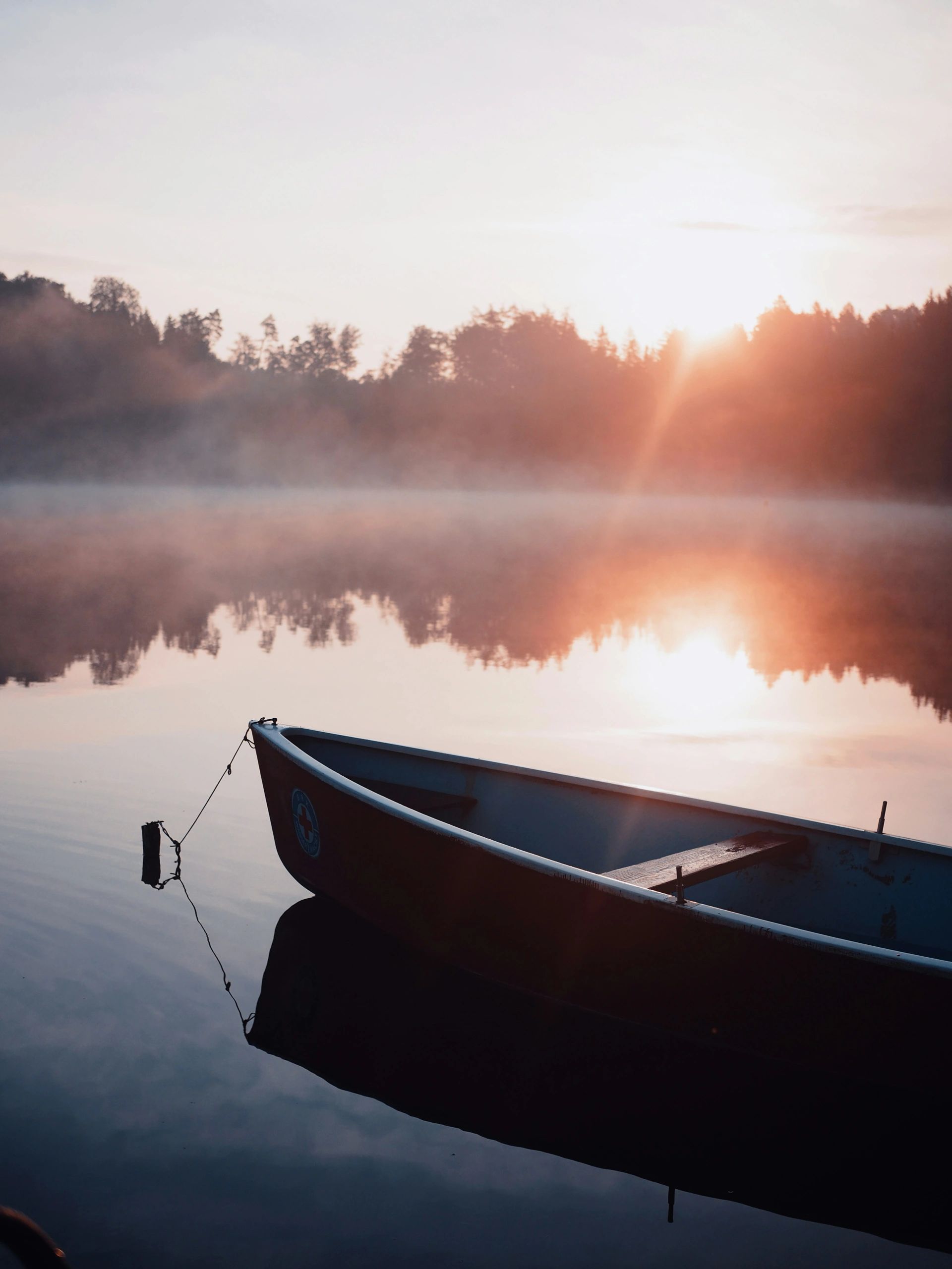 Boat resting on calm lake at sunrise, symbolising reflection, stillness, and new beginnings.