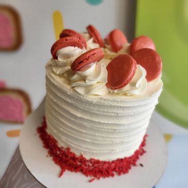 Red velvet cake with white icing, red sprinkles, and red macarons.
