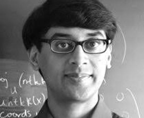 A man wearing glasses standing in front of a chalkboard with mathematical notations.