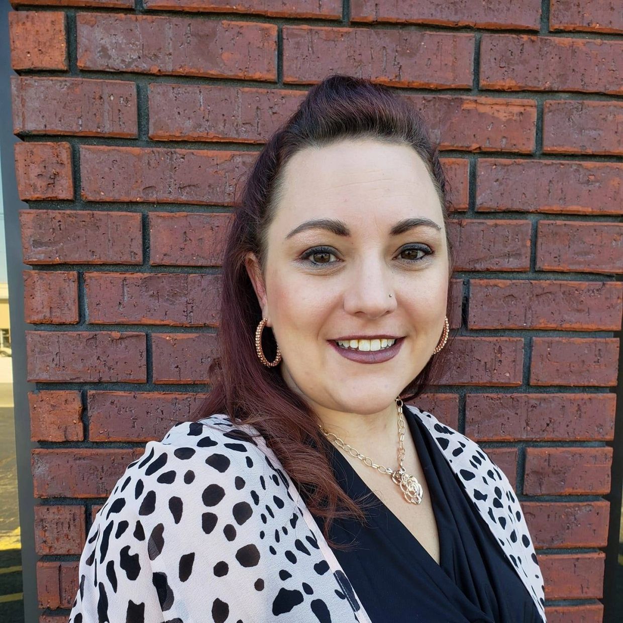 Smiling woman with hoop earrings in front of a brick wall.