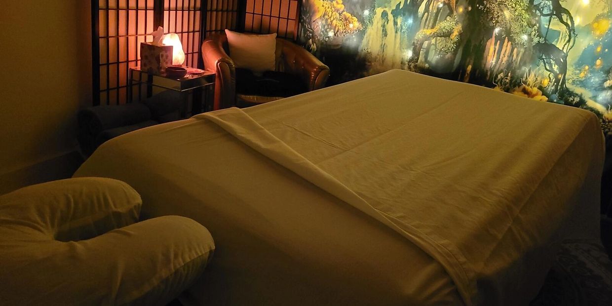 A cozy massage room with warm lighting and a mystical forest mural.