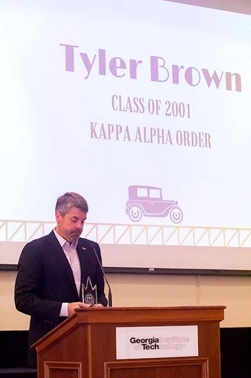 A man speaks at a podium with a presentation slide for Tyler Brown, Georgia Tech.