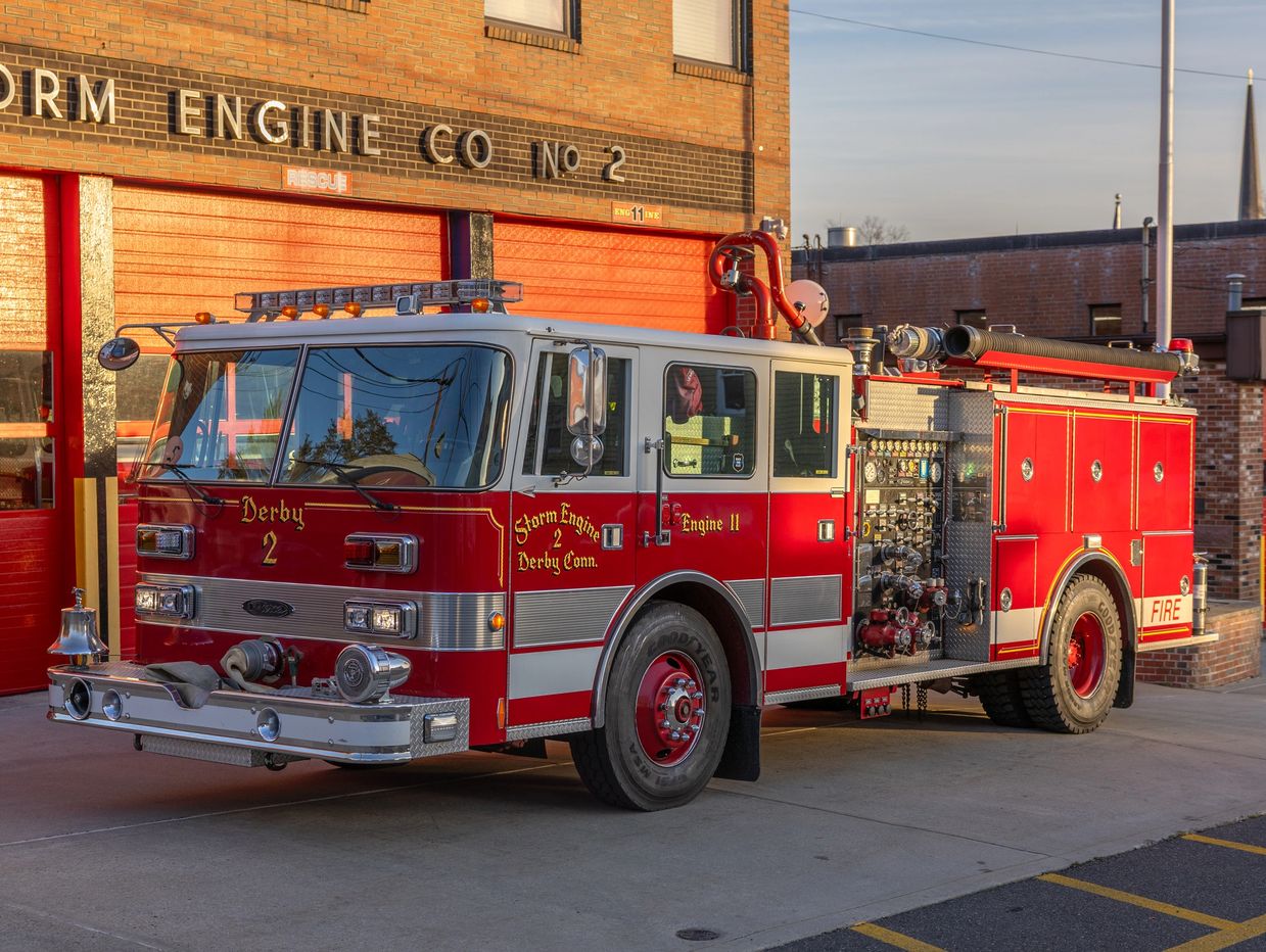 Red fire truck parked outside a fire station with red doors.