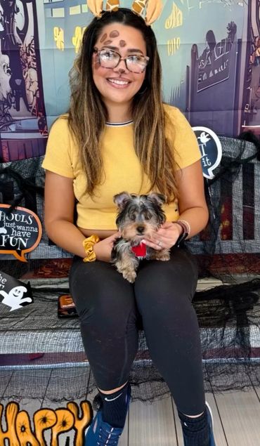 Young woman in giraffe costume holding a small dog, Halloween decorations around.