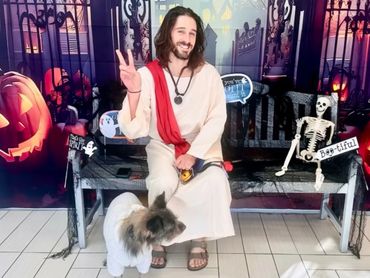 Man dressed as Jesus with a dog in sweater and Halloween decorations.
