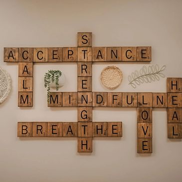 Wooden Scrabble tiles form positive words with small decorative plants on a beige wall.