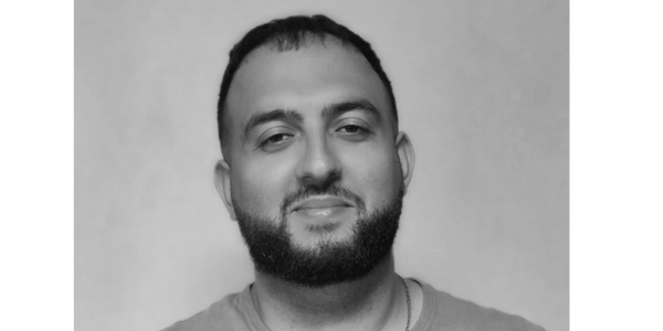 Smiling man with a beard in a blue t-shirt against a plain background.