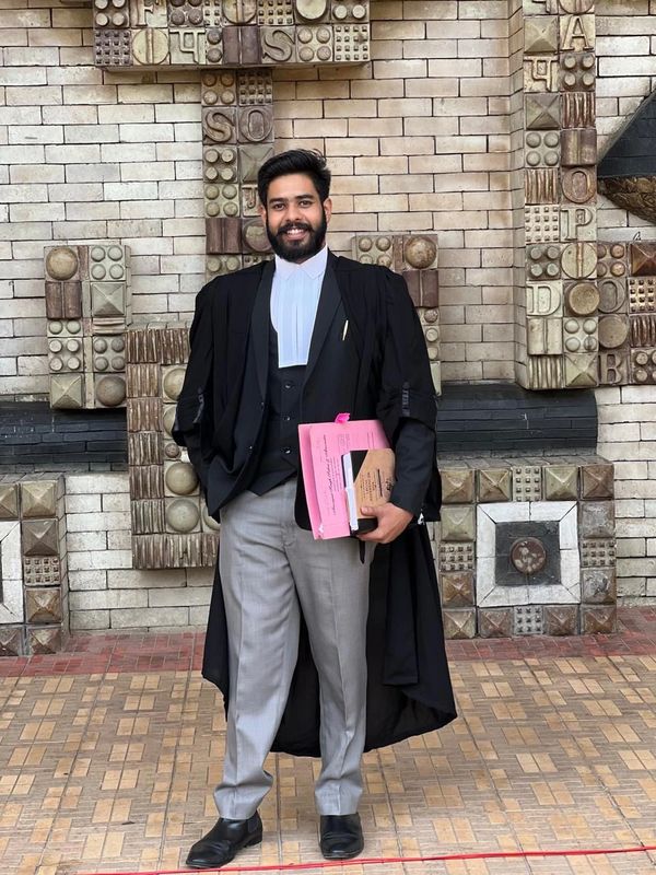 A man in formal legal attire holding documents and smiling.