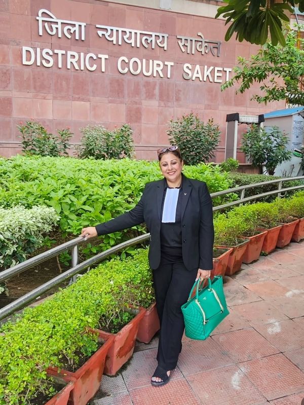 A woman dressed in black lawyer attire stands smiling at District Court Saket.