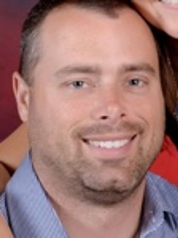 Smiling man in a blue shirt with a slight beard.