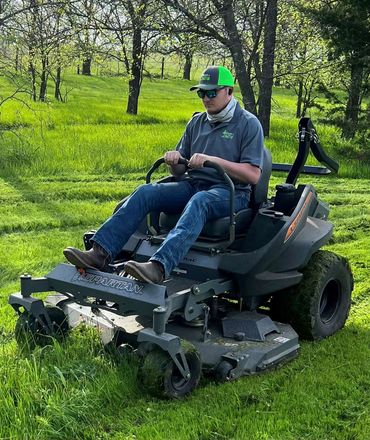 Man mowing grass on a Spartan lawn mower in a green field.