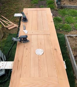 Wooden door being sanded outdoors with electric sanders.