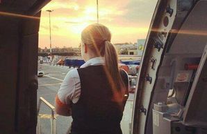 Flight attendant standing at an open door, looking at the sunset.