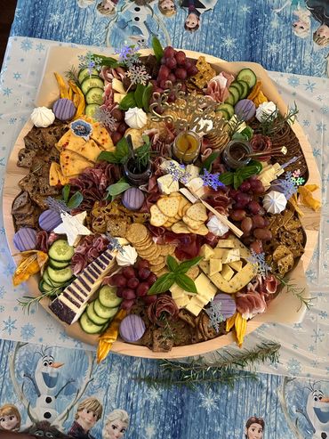 Colorful birthday charcuterie board with meats, cheeses, grapes, and crackers on Frozen-themed tablecloth.