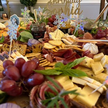Elegant birthday charcuterie board with cheeses, meats, grapes, crackers, and festive decorations.