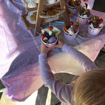 Child in purple sweater holding a cup of colorful snacks at a party table.