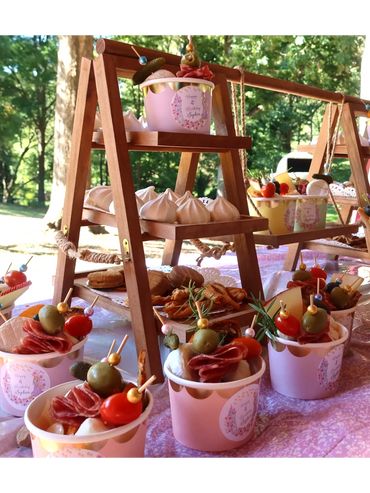 Elegant outdoor snack display with charcuterie cups and meringues on wooden shelves.
