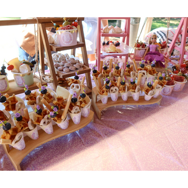 Colorful party snacks and sweets arranged on wooden stands with a doll decoration.