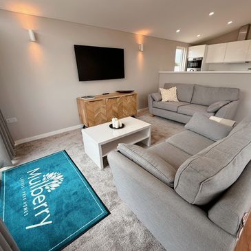 Modern living room with gray sofas, a wooden cabinet, and a wall-mounted TV in a Mulberry Lodge