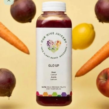 A bottle of Our Hive Juicery's Glo Up juice surrounded by fresh fruits and vegetables.