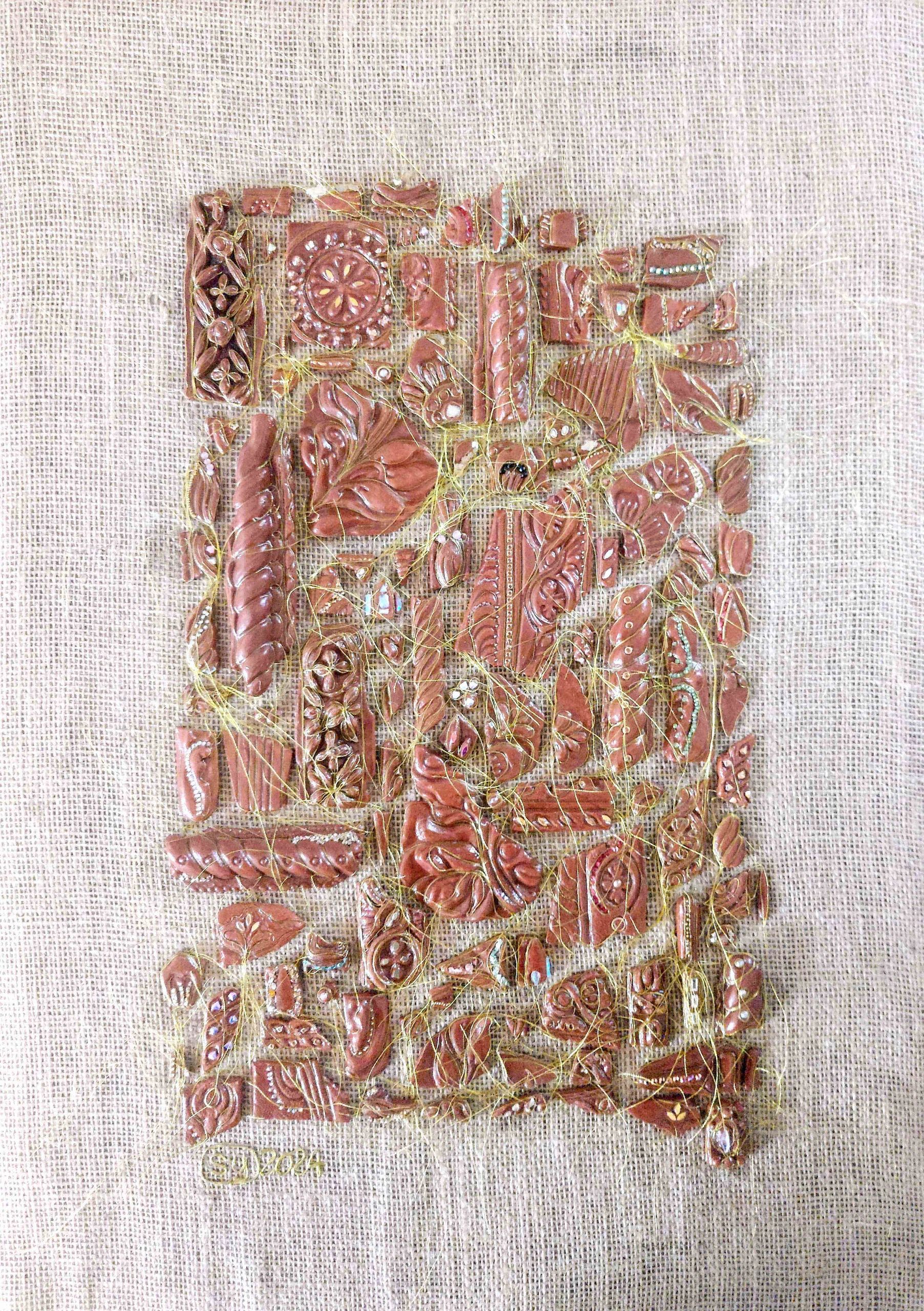 Terracotta greenware fragments arranged on jute-covered board with gold thread, embellishments and l