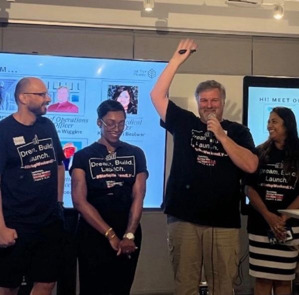 Four people in matching shirts speaking at an event with presentation screens behind them.
