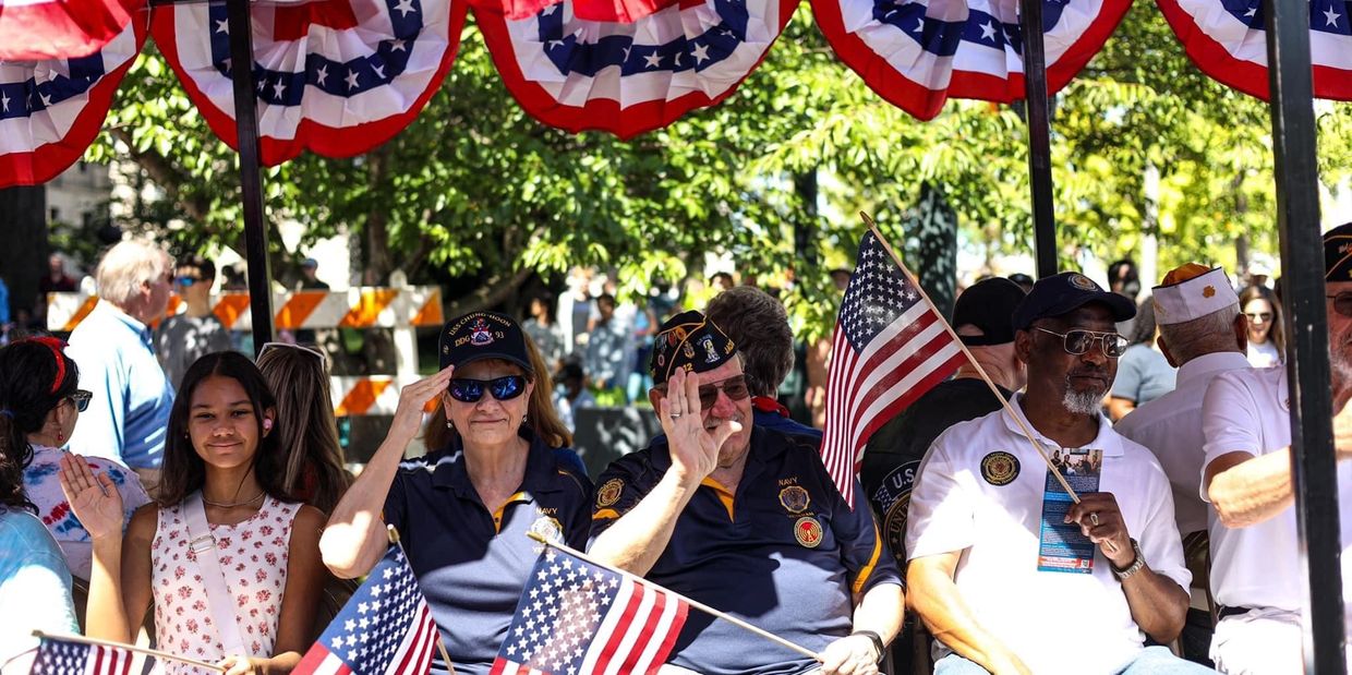 Veterans and a young girl salute and wave American flags during a patriotic event.