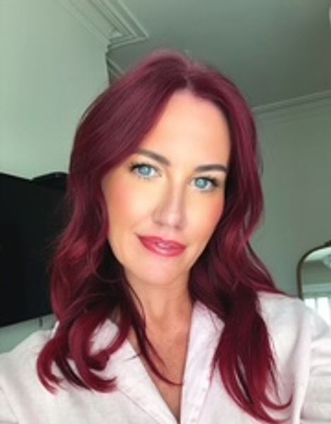 Woman with vibrant red hair and blue eyes smiling gently.