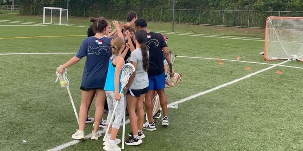 Youth lacrosse team gathers for a group cheer on the field.