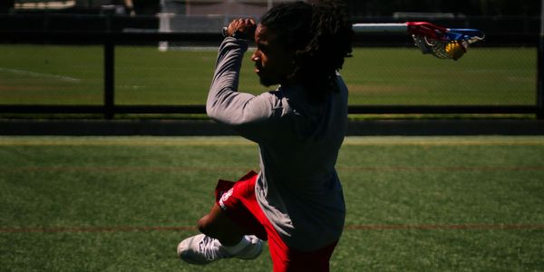 Athlete practicing lacrosse shot on a sunny field.