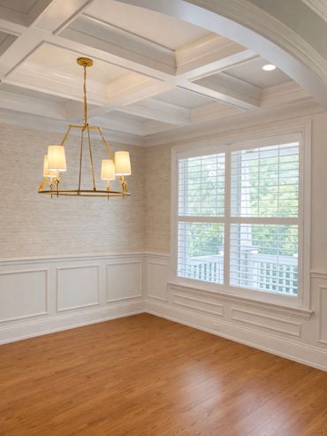 Elegant empty dining room with wooden floor, white walls, and gold chandelier.